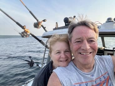 A couple enjoying a scenic moment on a fishing boat, with fishing rods visible in the background, highlighting a relaxed fishing atmosphere.