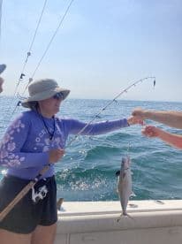 A young angler reeling in a fish while fishing on a boat in open waters, showcasing an exciting moment during a fishing trip.