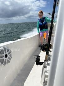 A young angler enjoying the thrill of fishing aboard a boat, with fishing gear visible and the ocean in the background.