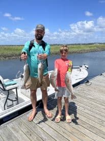 A proud father and son duo displaying their catch of Redfish after a successful day of fishing in a coastal environment.