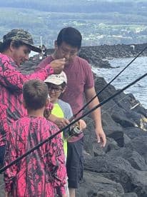A group of young anglers learning to fish from experienced guides on rocky shores, showcasing a hands-on fishing experience.