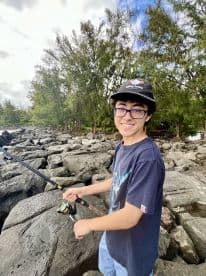 A young angler casting a fishing rod on rocky terrain, surrounded by lush greenery, showcasing the excitement of fishing in a natural setting.