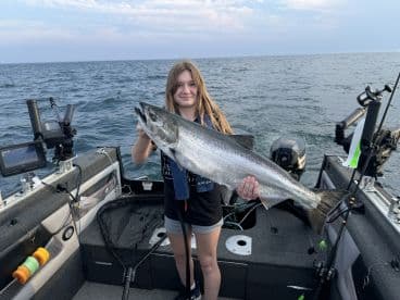 A young angler proudly displaying a large Salmon while fishing on a boat in open waters.