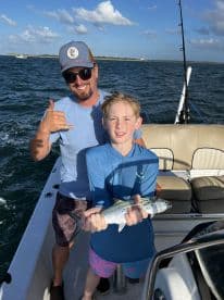 A young angler proudly displaying a Spanish Mackerel while fishing with an adult on a boat, enjoying a sunny day on the water.