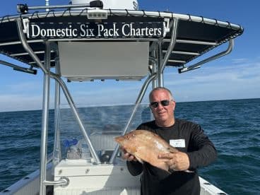 Angler proudly displaying a large Snapper aboard a charter boat in open waters.
