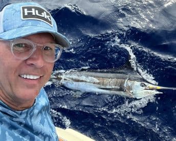 An angler captures a selfie while reeling in a large Marlin during a deep-sea fishing adventure.