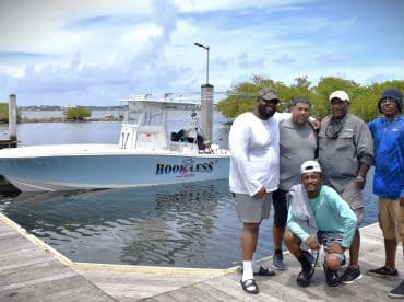 A group of five anglers posing in front of the 'Hookless II' boat at the dock, showcasing a beautiful day on the water.