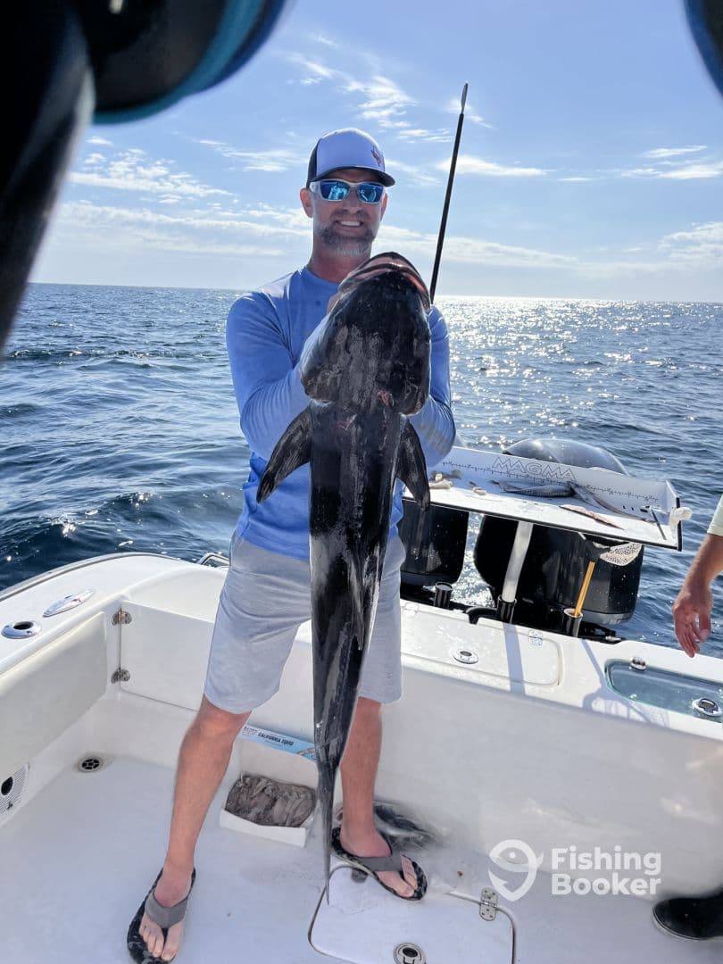 Angler proudly displaying a large Black Grouper while fishing offshore, showcasing a sunny day on the water.