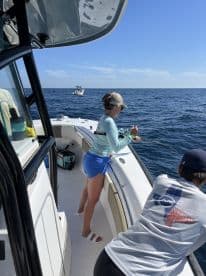 A young angler is actively reeling in a fish while fishing on a boat in open water, showcasing the excitement of the sport.