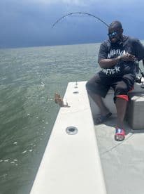 Angler reeling in a fish while enjoying a sunny day on the water, showcasing the excitement of fishing.