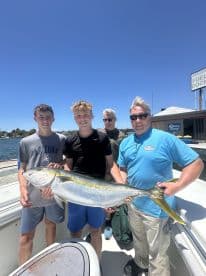 Group of young anglers proudly displaying a large Yellowtail caught during a fishing trip, with a scenic harbor backdrop.