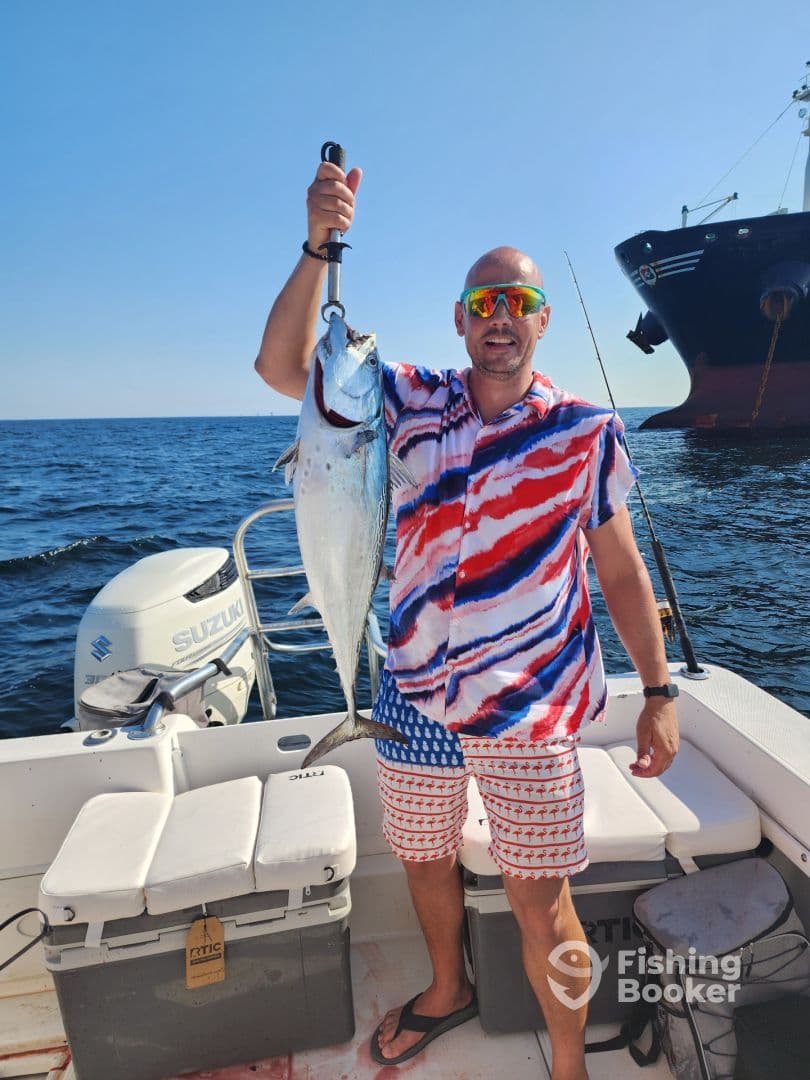 Angler proudly displaying a large fish while aboard a fishing boat in open waters, showcasing a vibrant summer outfit.