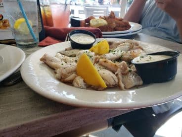 A plate of freshly prepared fish fillets garnished with lemon and served with dipping sauces, enjoyed at a casual dining setting.