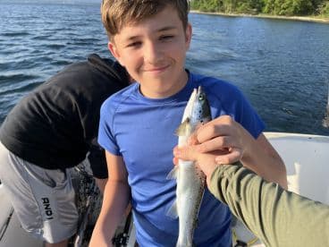 A young angler proudly displaying a caught fish while fishing on a boat, surrounded by water and greenery.