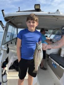 A young angler proudly displaying a caught trout while aboard a fishing boat, showcasing a successful day on the water.