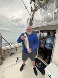 An angler proudly displaying a large fish on a charter boat, with fellow passengers visible in the background.