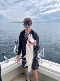 A young angler proudly displaying a freshly caught fish while aboard a fishing boat, showcasing a successful day on the water.