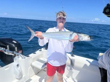 A young angler proudly displaying a large King Mackerel while fishing on a boat in open waters.