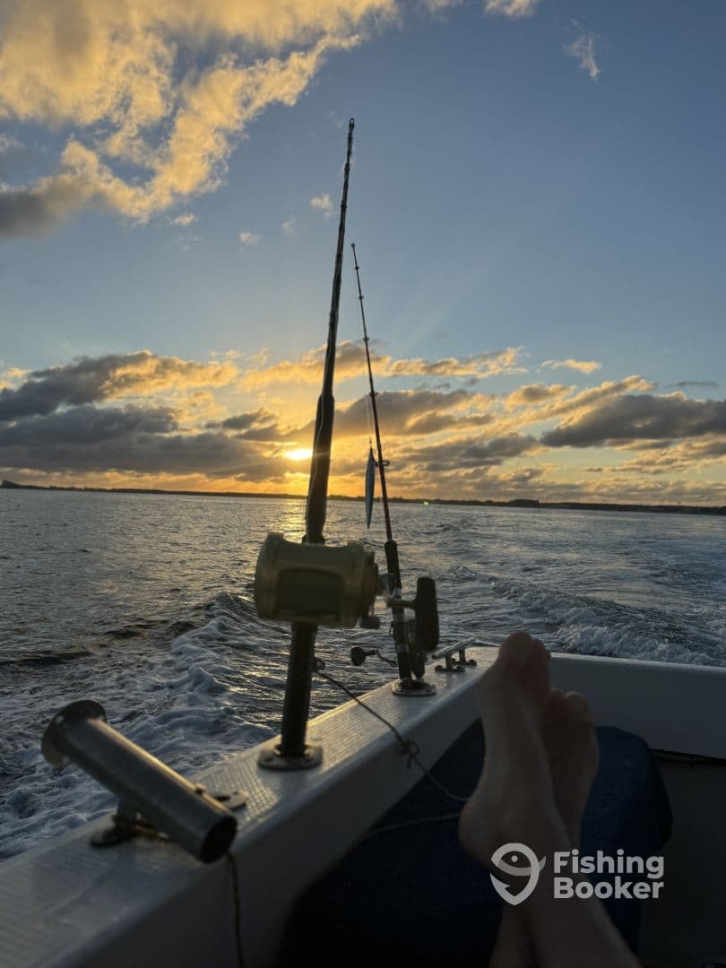 A serene sunset view from the interior of a fishing boat, showcasing fishing rods and a relaxed angler's feet.