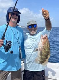 Two anglers proudly displaying a large Grouper caught during a deep-sea fishing trip.
