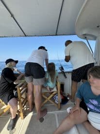 A family enjoying a fishing trip on a boat, with a child and adults engaged in fishing activities, overlooking the calm sea.
