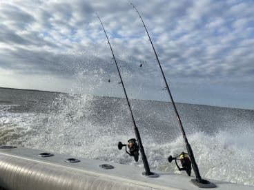 Fishing rods are set up on a boat as water splashes around, capturing the excitement of a fishing trip in a scenic waterway.