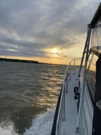 A scenic view of a boat cruising on the water during sunset, showcasing the boat's exterior and the tranquil fishing environment.
