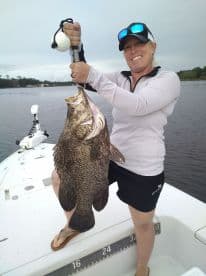 An angler proudly displaying a large Grouper caught while fishing on a boat in calm waters.
