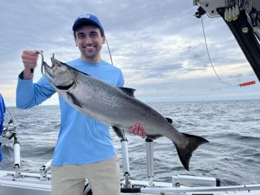 An angler proudly displaying a large Salmon while fishing offshore, showcasing the excitement of a successful catch.