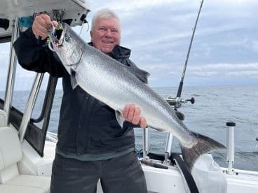An angler proudly displaying a large Salmon aboard a fishing boat, showcasing a successful day on the water.