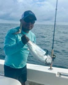 Angler holding a shiny fish while fishing offshore, showcasing a successful catch during a deep-sea fishing trip.
