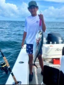A young angler proudly displaying a large fish while aboard a fishing boat in open waters, showcasing a successful catch.