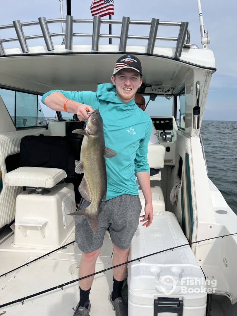 A young angler proudly displaying a large Catfish aboard a fishing boat, showcasing a successful day on the water.
