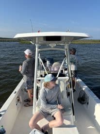 A group of anglers enjoying a day on a center console boat, with one young angler seated and others preparing to fish in a scenic coastal environment.