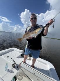 An angler proudly displaying a large Redfish while fishing on a sunny day in a calm waterway.