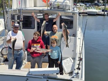 A family proudly displaying their catch of striped bass aboard a fishing charter, showcasing a successful day on the water.