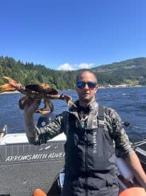 Angler proudly displaying a large Dungeness crab while on a fishing adventure in a scenic coastal environment.
