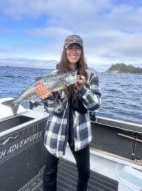 A proud angler holding a beautiful Salmon while fishing on a boat in a scenic coastal environment.