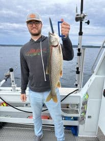 Angler proudly displaying a large Lake Trout while fishing on a boat, showcasing a successful day on the water.
