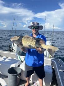 Angler displaying a large Grouper while fishing on a boat in open waters, showcasing a successful day on the water.