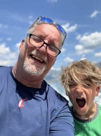 A joyful moment captured between an adult and a child, both smiling and enjoying their time outdoors, likely on a fishing trip.