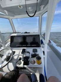 Interior view of a modern fishing boat's helm, showcasing the control panel and seating arrangement while navigating on calm waters.