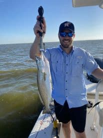 An angler proudly displaying a large Speckled Trout while fishing on a boat in coastal waters.