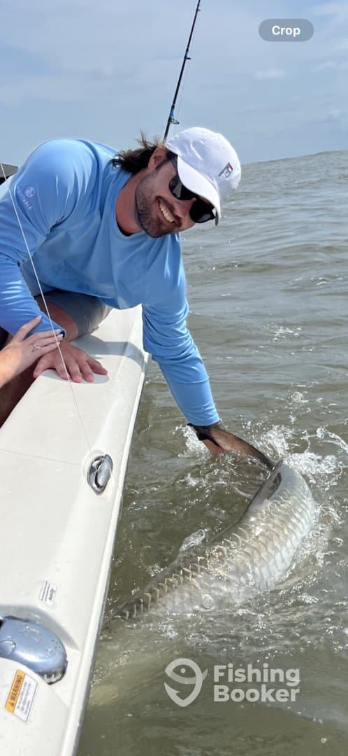 Angler reeling in a large Tarpon while fishing from a boat in coastal waters, showcasing an exciting moment in sport fishing.