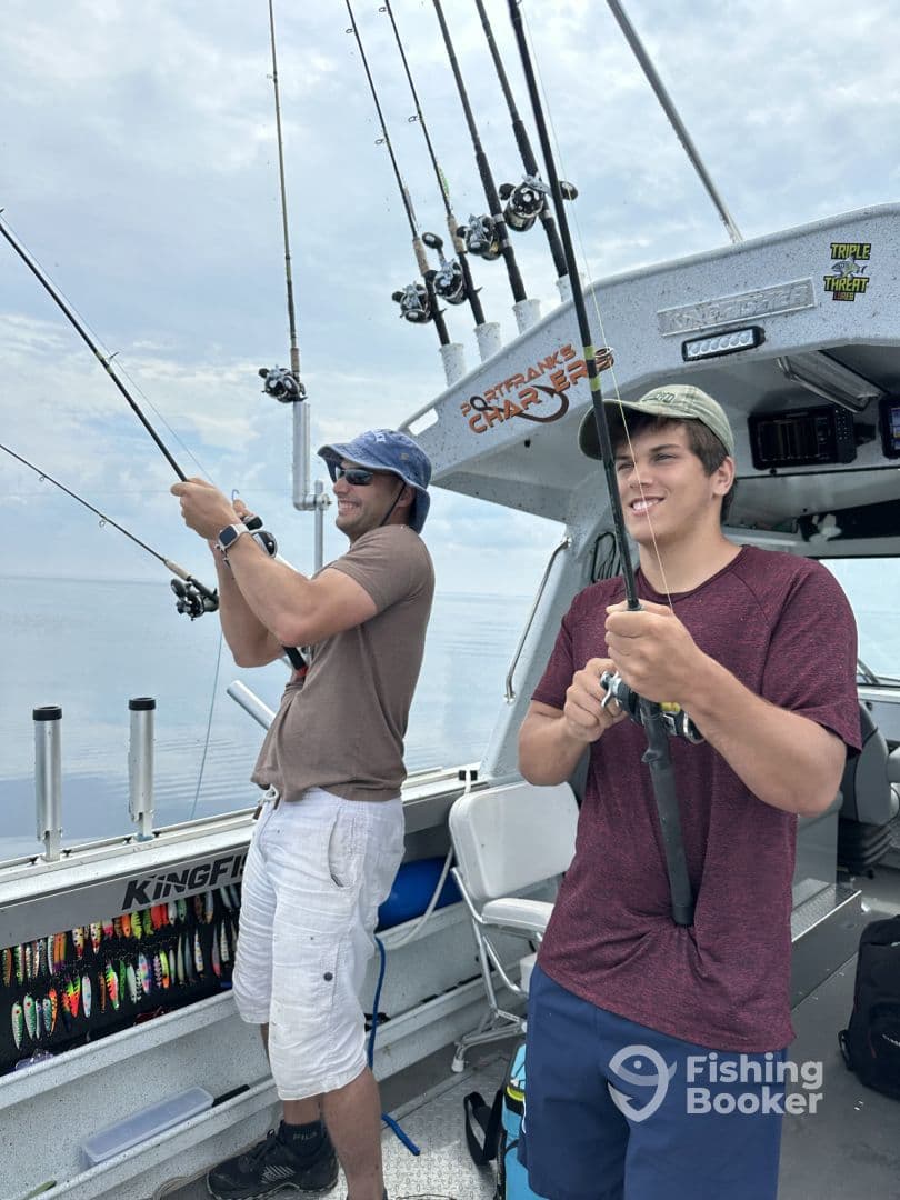 Two anglers actively reeling in their lines while fishing on a charter boat, showcasing a lively fishing environment.