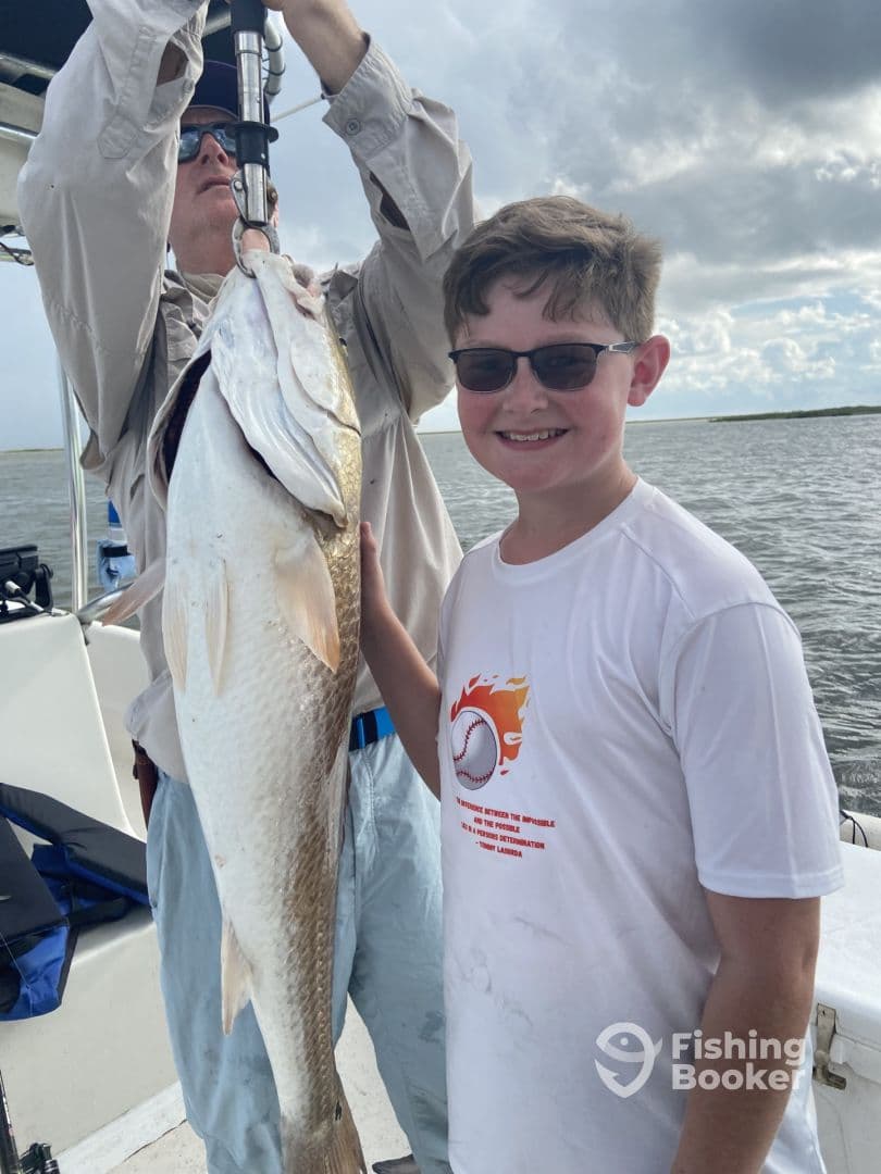 A young angler proudly displays a large Redfish while fishing on a boat, showcasing a successful day on the water.