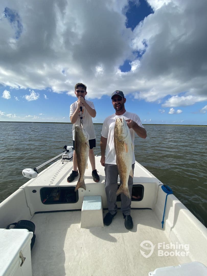 A young angler and an adult proudly displaying their catch of two large Redfish while on a fishing trip.
