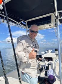 Captain smiling at the helm of a fishing boat, showcasing the interior setup and sunny weather.
