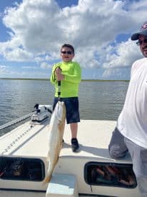 A young angler proudly displaying a large Redfish while fishing on a sunny day in a coastal waterway.