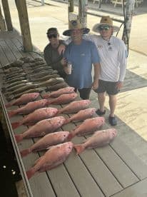 A group of anglers proudly displaying their catch of Red Snapper and other species on a dock after a successful fishing trip.